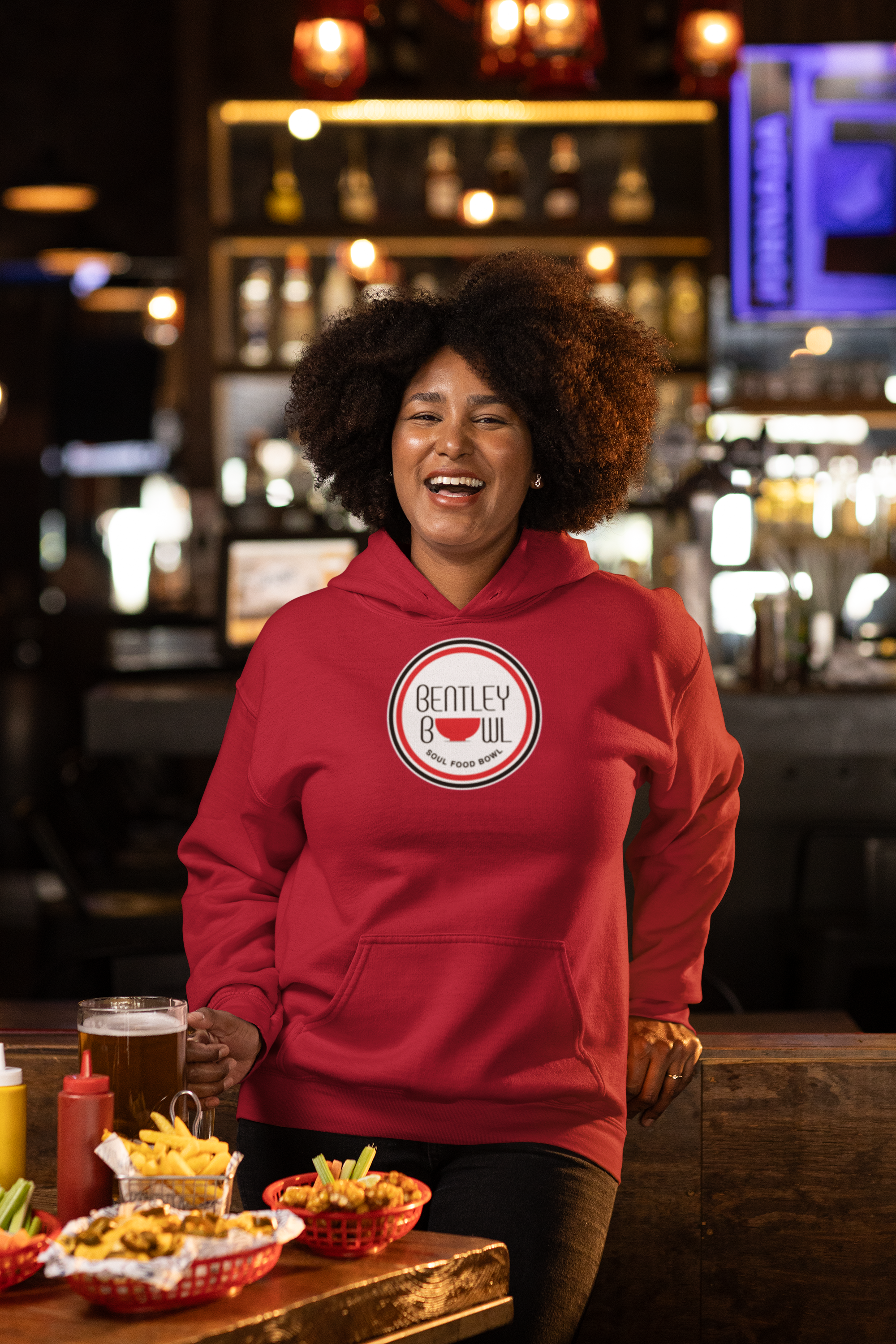 files/gildan-pullover-hoodie-mockup-of-a-happy-woman-having-food-and-drinks-in-a-sports-bar-m38089.png